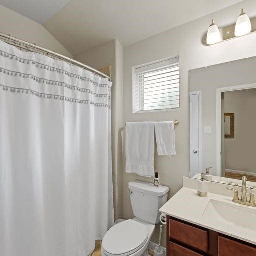 bathroom with toilet, vanity, and vaulted ceiling