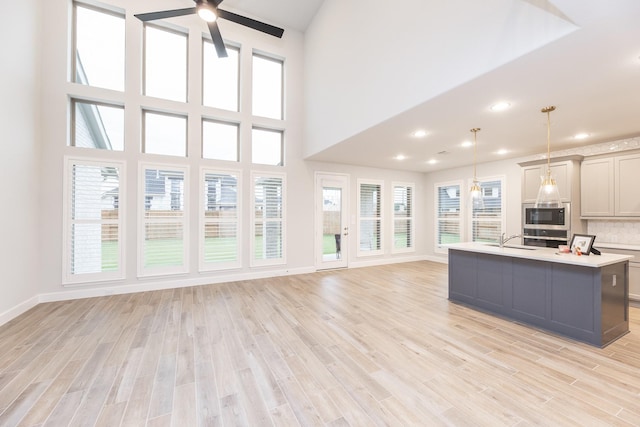 kitchen with stainless steel appliances, sink, gray cabinets, hanging light fixtures, and an island with sink