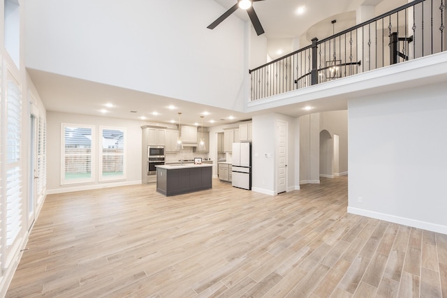 unfurnished living room featuring ceiling fan, light hardwood / wood-style floors, sink, and a high ceiling