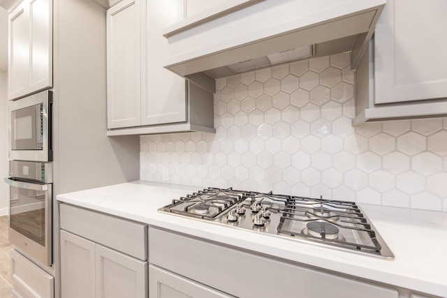 kitchen featuring white cabinets, stainless steel appliances, tasteful backsplash, and range hood