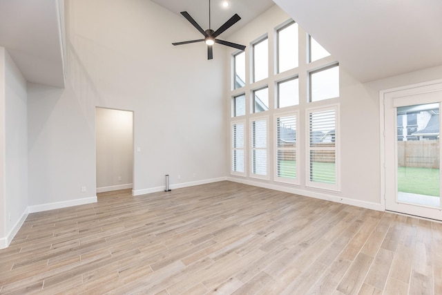 unfurnished living room with ceiling fan, light wood-type flooring, and a towering ceiling