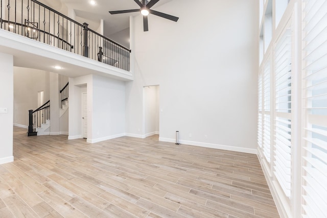 unfurnished living room featuring ceiling fan, light hardwood / wood-style flooring, and a high ceiling