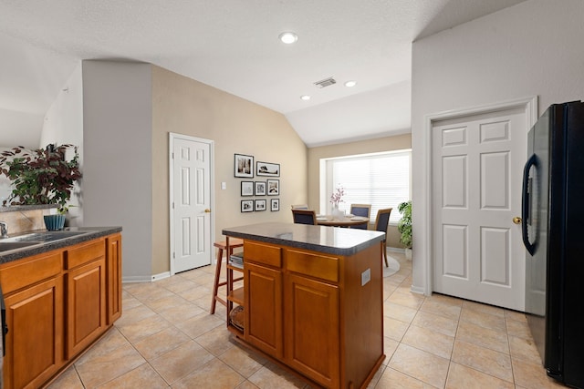 kitchen with black fridge, a center island, light tile patterned floors, and vaulted ceiling