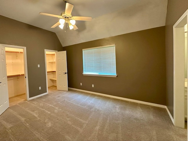 unfurnished bedroom with carpet flooring, a walk in closet, ceiling fan, a closet, and lofted ceiling