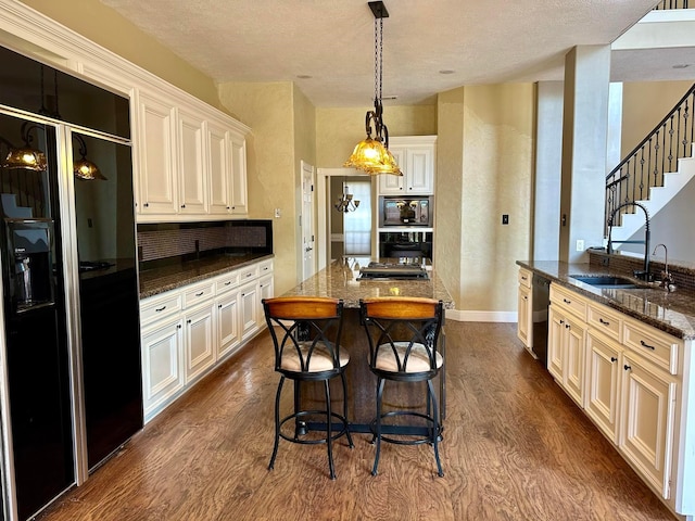 kitchen with sink, dark hardwood / wood-style flooring, dark stone countertops, a kitchen island with sink, and black appliances