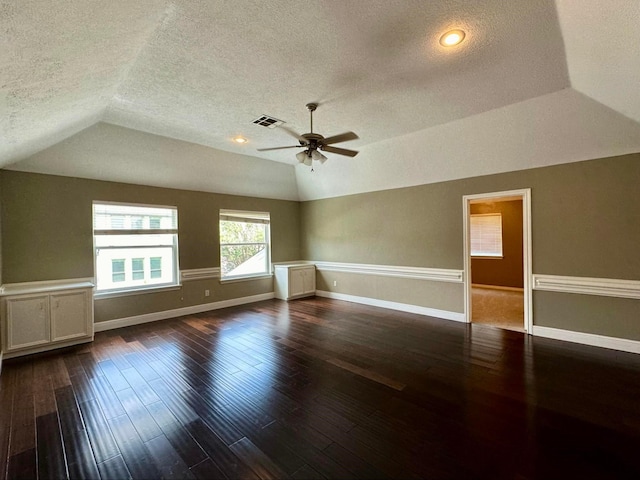 empty room with dark wood-type flooring, a raised ceiling, vaulted ceiling, ceiling fan, and a textured ceiling