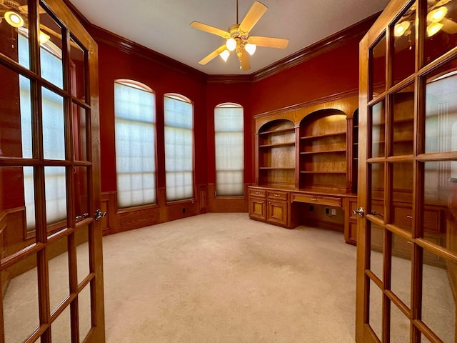 home office featuring ceiling fan, crown molding, built in desk, and light carpet