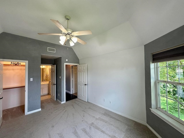 unfurnished bedroom featuring ceiling fan, light colored carpet, connected bathroom, and vaulted ceiling