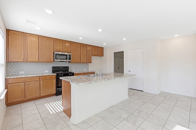 kitchen featuring decorative backsplash, black range oven, sink, light tile patterned floors, and an island with sink