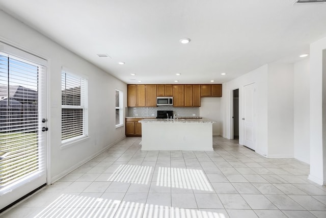 kitchen featuring backsplash, sink, light stone countertops, light tile patterned floors, and an island with sink