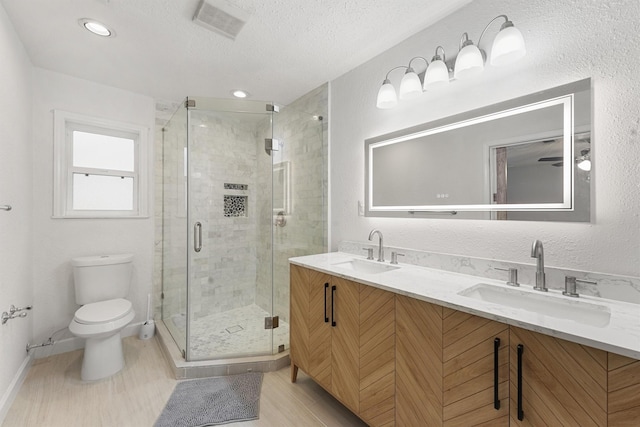 bathroom featuring a textured ceiling, vanity, toilet, and a shower with shower door