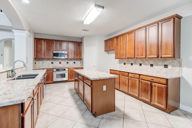 kitchen with sink, a center island, stainless steel appliances, light stone counters, and light tile patterned floors