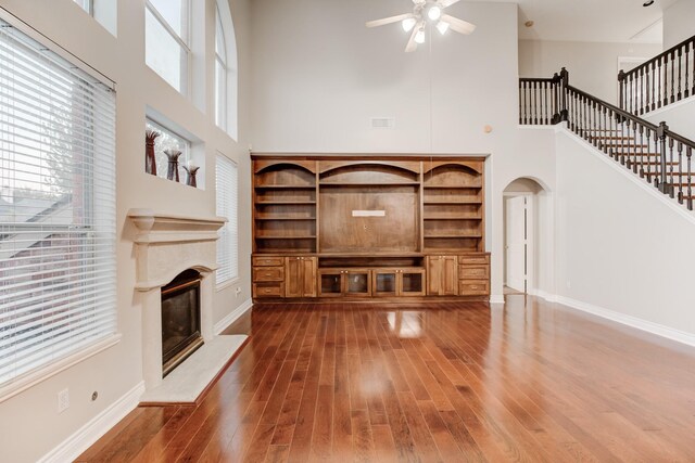 unfurnished living room with ceiling fan, a towering ceiling, and dark wood-type flooring