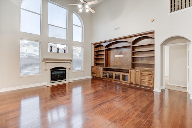 unfurnished living room featuring ceiling fan, hardwood / wood-style floors, and a towering ceiling