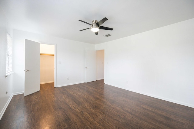 unfurnished bedroom with a closet, a walk in closet, ceiling fan, and dark hardwood / wood-style flooring