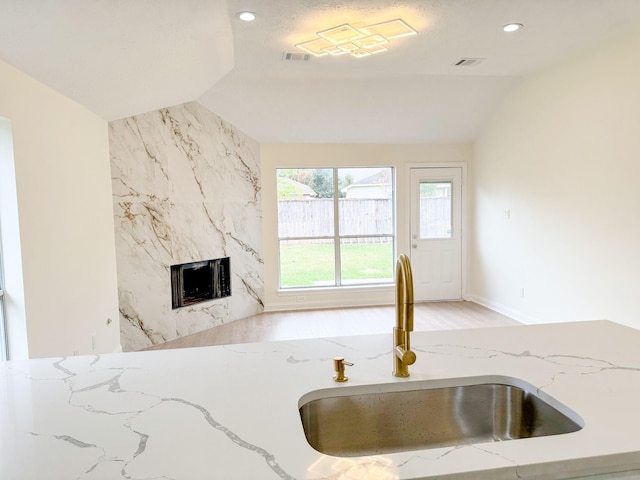 kitchen with light stone counters, lofted ceiling, sink, and a high end fireplace