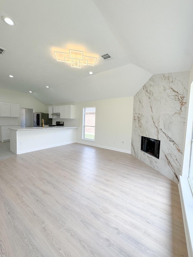 unfurnished living room with a fireplace, light hardwood / wood-style floors, and vaulted ceiling