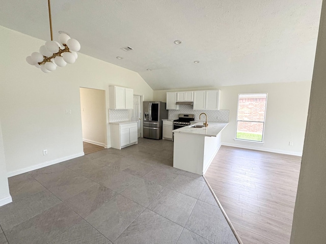 kitchen with appliances with stainless steel finishes, backsplash, vaulted ceiling, sink, and white cabinets