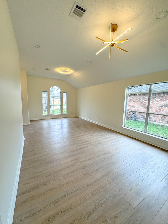 spare room featuring a notable chandelier, light wood-type flooring, a textured ceiling, and vaulted ceiling