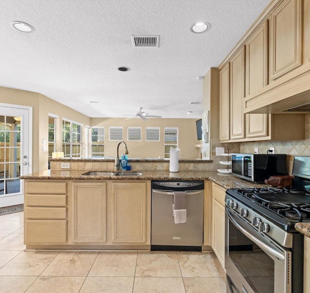 kitchen with kitchen peninsula, stainless steel appliances, sink, light tile patterned floors, and stone countertops