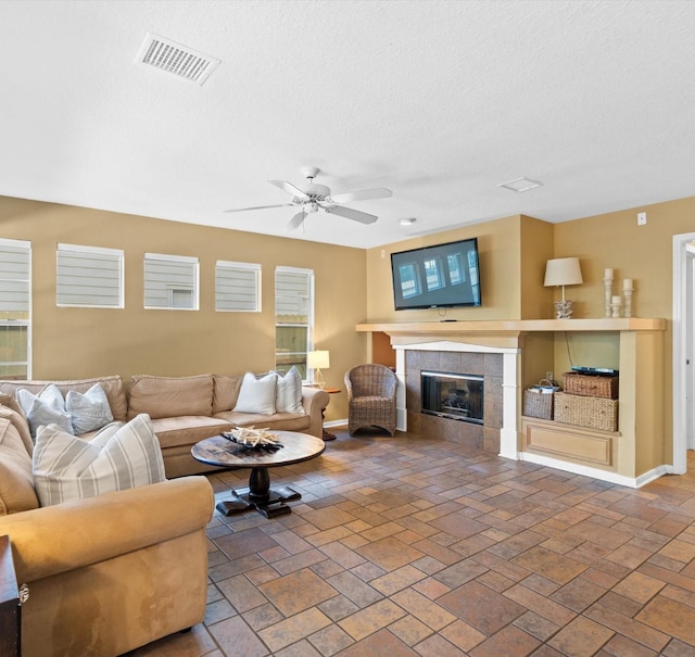 living room featuring a textured ceiling, ceiling fan, and a tiled fireplace