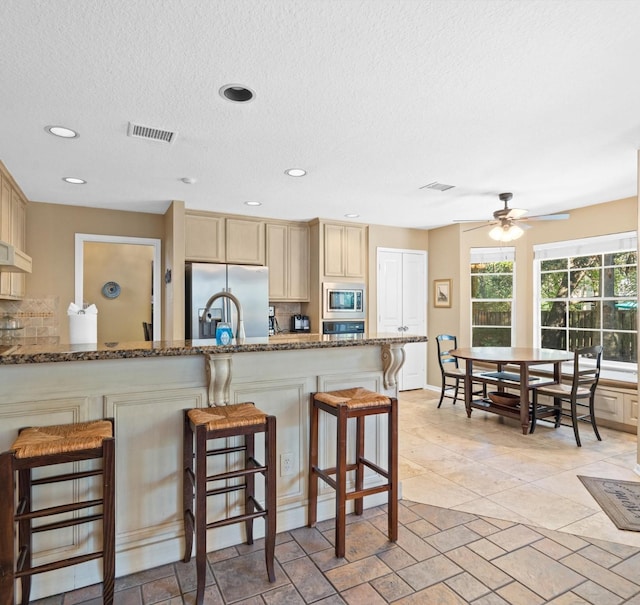 kitchen featuring stone counters, ceiling fan, stainless steel appliances, backsplash, and a kitchen bar