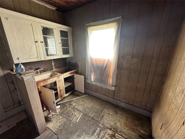 kitchen featuring white cabinets, wood walls, and sink