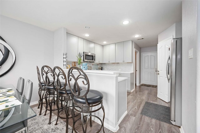 kitchen featuring white cabinetry, a kitchen breakfast bar, backsplash, kitchen peninsula, and appliances with stainless steel finishes