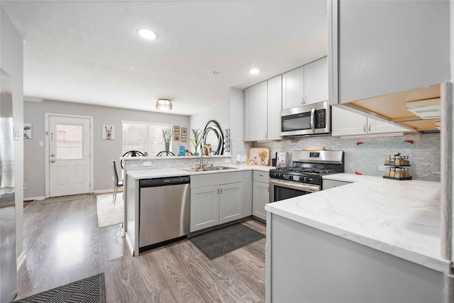 kitchen featuring sink, light stone countertops, tasteful backsplash, kitchen peninsula, and stainless steel appliances