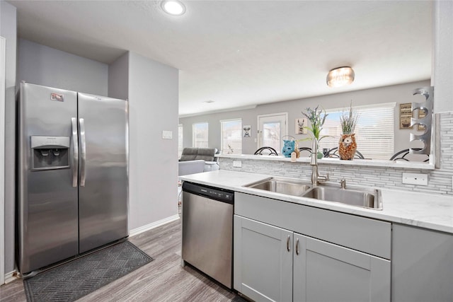 kitchen with appliances with stainless steel finishes, light stone counters, sink, light hardwood / wood-style flooring, and gray cabinets