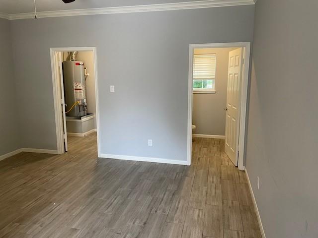 unfurnished bedroom with a walk in closet, gas water heater, wood-type flooring, and ornamental molding