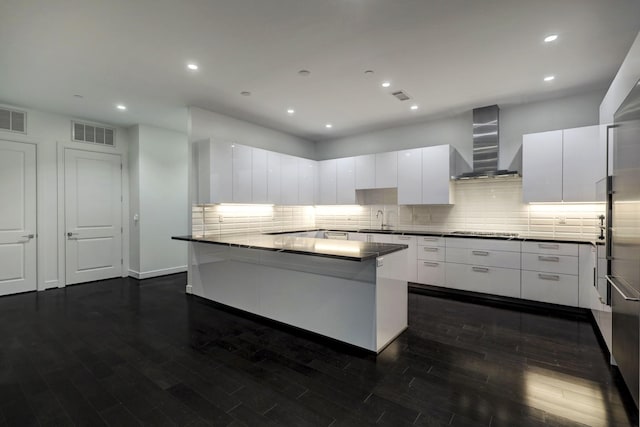 kitchen with a center island, wall chimney range hood, sink, white cabinetry, and gas cooktop