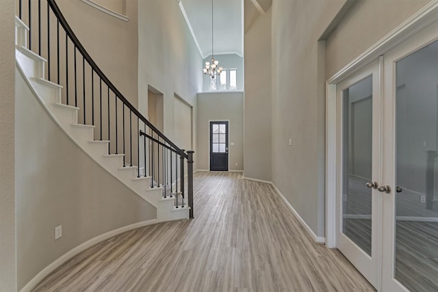 entryway featuring french doors, a high ceiling, a notable chandelier, crown molding, and light hardwood / wood-style floors