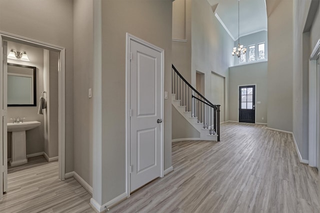 foyer entrance with light wood-type flooring, a towering ceiling, ornamental molding, sink, and a notable chandelier