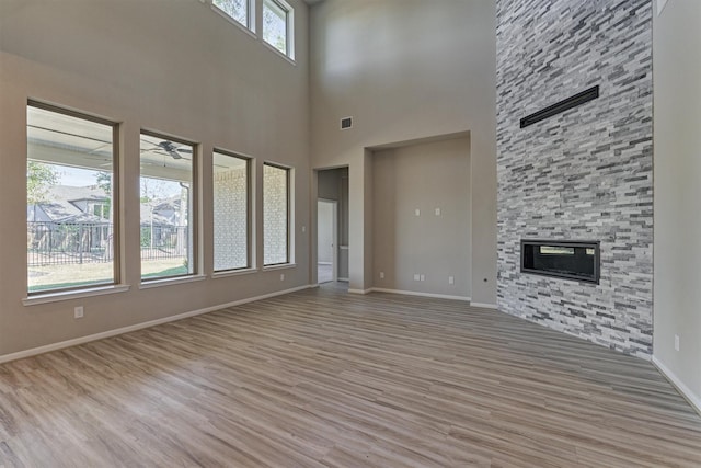 unfurnished living room featuring a fireplace, a towering ceiling, light hardwood / wood-style flooring, and ceiling fan