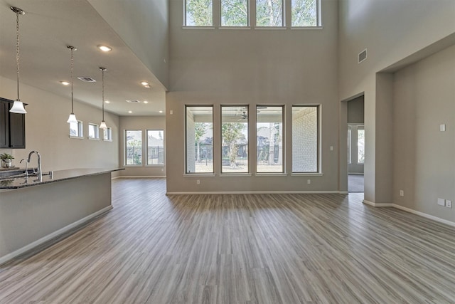 unfurnished living room with a towering ceiling, light wood-type flooring, and sink