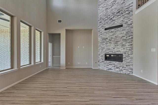 unfurnished living room with a fireplace, a high ceiling, and light wood-type flooring