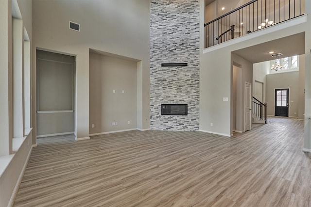 unfurnished living room with light wood-type flooring, a towering ceiling, and a stone fireplace