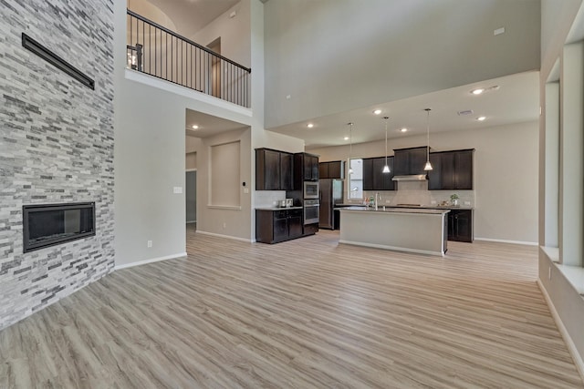 unfurnished living room featuring a large fireplace, a towering ceiling, light hardwood / wood-style floors, and sink