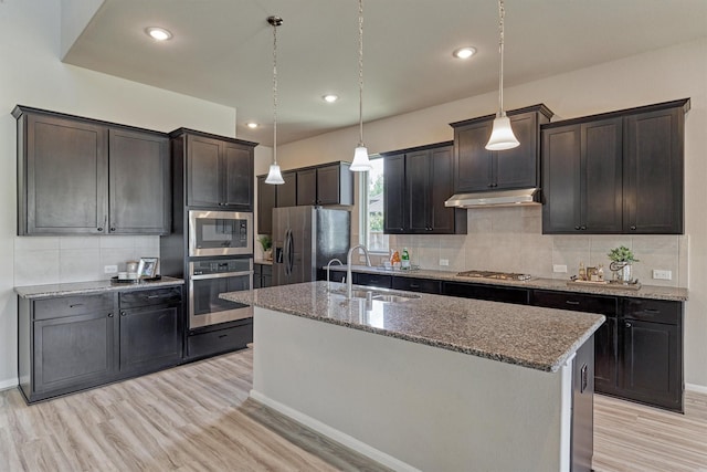 kitchen with pendant lighting, backsplash, stainless steel appliances, and a kitchen island with sink