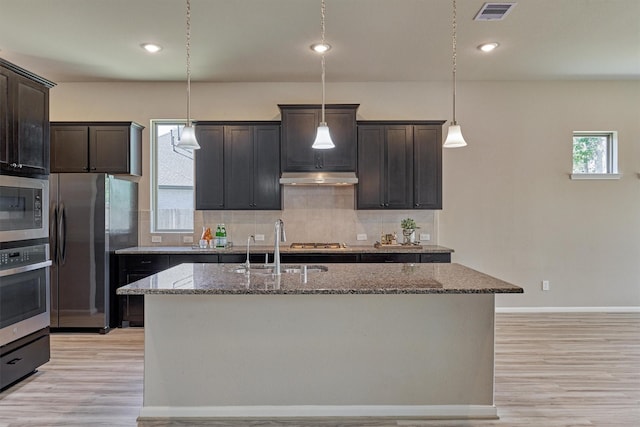 kitchen with light stone countertops, dark brown cabinetry, a kitchen island with sink, and appliances with stainless steel finishes