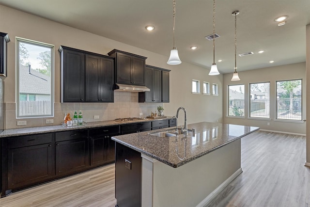 kitchen featuring pendant lighting, a kitchen island with sink, sink, light hardwood / wood-style flooring, and tasteful backsplash