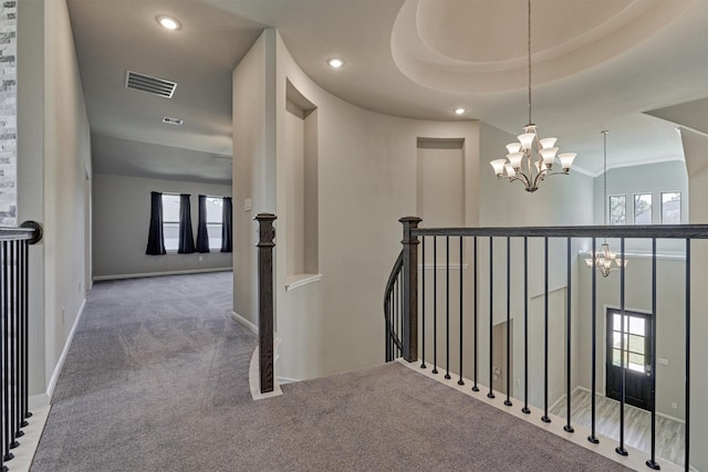 hall with carpet floors, a raised ceiling, and a notable chandelier