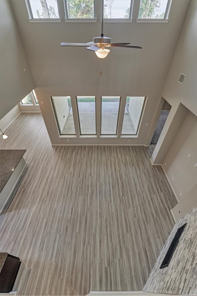 unfurnished living room with ceiling fan, light hardwood / wood-style flooring, and a high ceiling