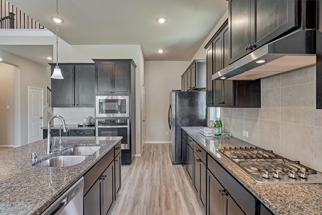 kitchen featuring ventilation hood, sink, dark stone countertops, appliances with stainless steel finishes, and decorative light fixtures