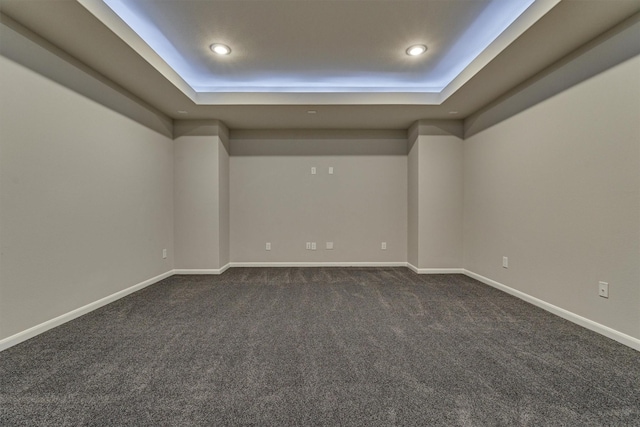 empty room featuring dark colored carpet and a tray ceiling