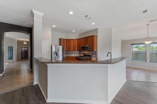 kitchen with pendant lighting, kitchen peninsula, stainless steel appliances, and light hardwood / wood-style flooring