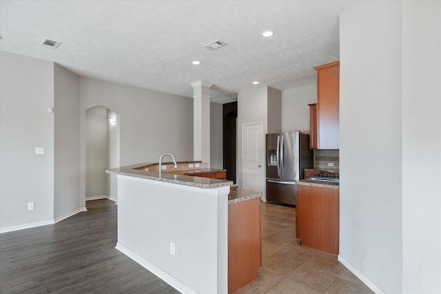 kitchen with light stone counters, a textured ceiling, light tile patterned floors, a center island with sink, and stainless steel fridge with ice dispenser