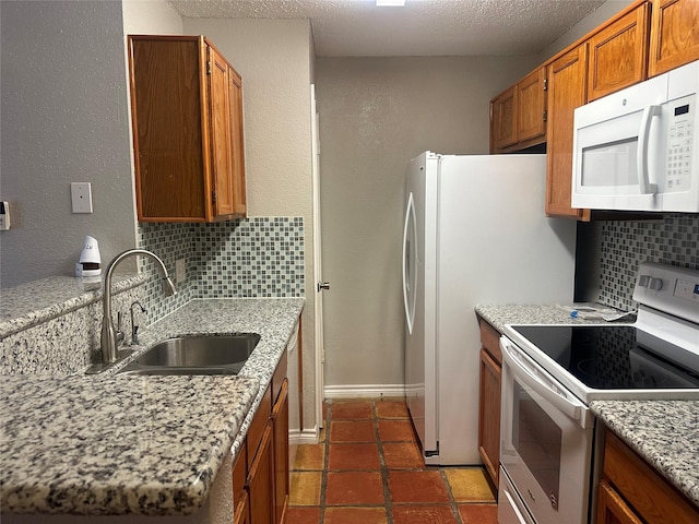 kitchen featuring light stone countertops, white appliances, tasteful backsplash, and sink