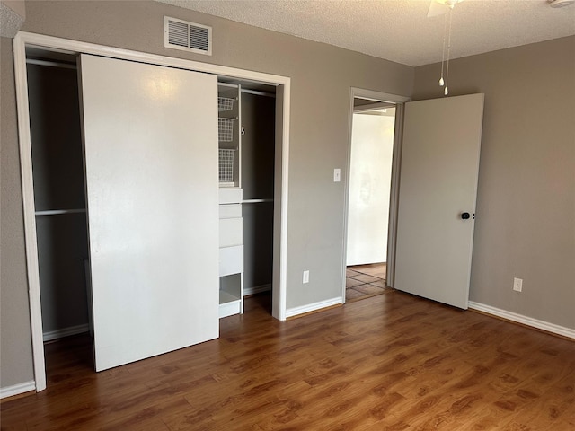 unfurnished bedroom featuring a textured ceiling, a closet, dark wood-type flooring, and ceiling fan